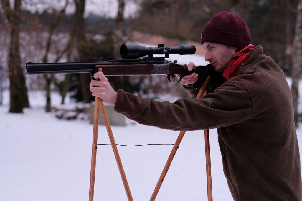 Jäger im sicheren Anschlag mit dem Pirschstock aus Holz bei der Winterjagd